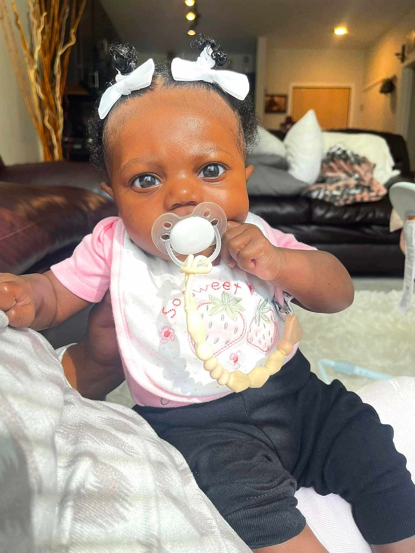Audri joined the competition — help win amazing prizes! baby, infant, pacifier, hair_bows, pink_shirt, black_pants, living_room, couch, pillows, blanket, beads, child, cute, portrait, indoor, person, hand, skin, expression, comfort