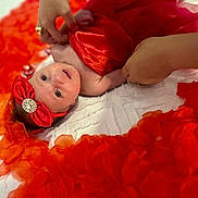 Charlotte is registered to the contest to win money with this photo: baby, infant, red_bow, headband, red_cloth, flower_petals, white_bedspread, hands, rings, portrait, newborn, cute, lying_down, soft_lighting, closeup, skin, decorative, colorful, celebration, adorable