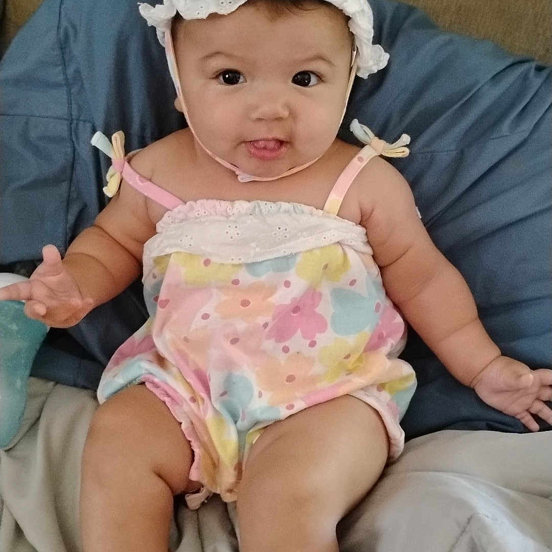 Pyper is registered to the contest to win money with this photo: baby, infant, child, romper, bonnet, pastel_colors, cute, smiling, tongue_out, sitting, bed, blanket, cushion, indoors, person, plush, happy, skin, headwear, casual