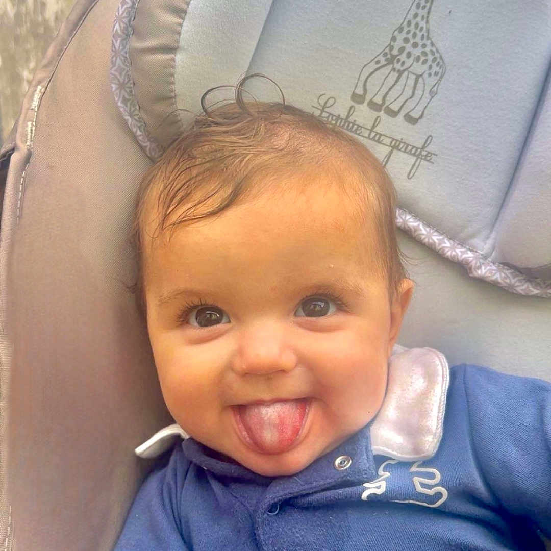 Timélyo participe au concours pour gagner de l'argent avec cette photo : baby, baby_seat, blue_clothing, child, closeup, cute, face, giraffe_illustration, happy, head, indoors, infant, padded_seat, person, playful, portrait, smiling, soft_toys, tongue_out, young_child