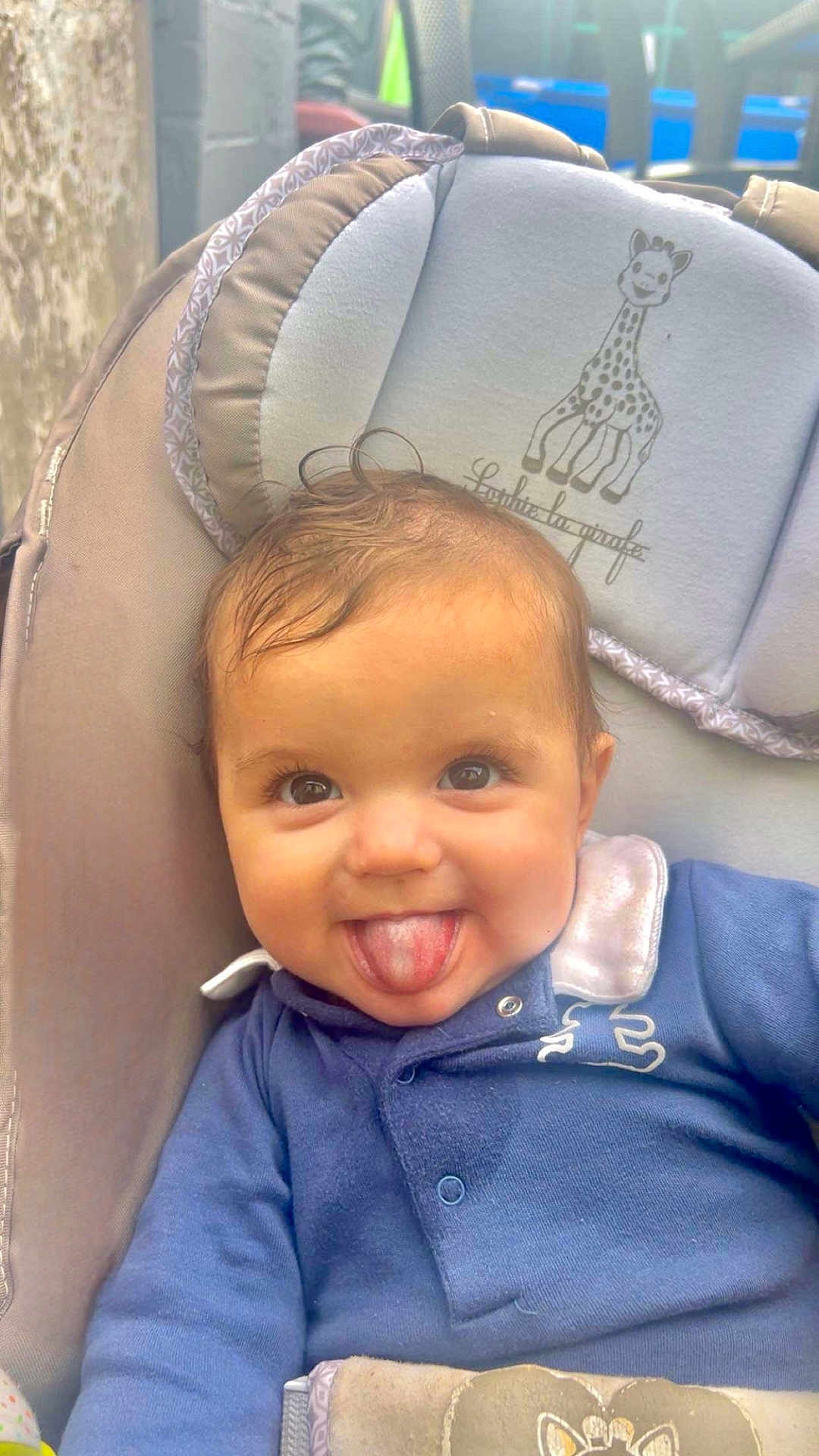 Timélyo participe au concours pour gagner de l'argent avec cette photo : baby, child, tongue_out, smiling, blue_clothing, baby_seat, giraffe_illustration, cute, playful, infant, face, head, person, indoors, soft_toys, padded_seat, happy, young_child, closeup, portrait