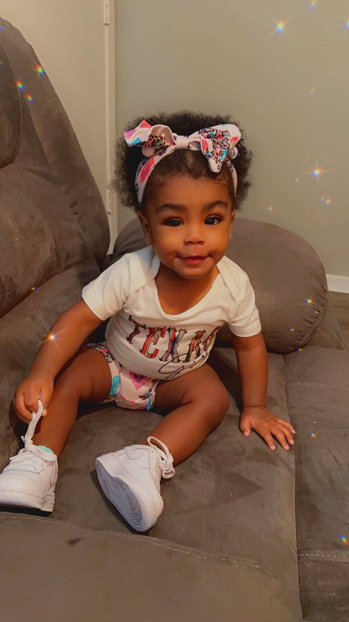 Tahiri is registered to the contest to win money with this photo: baby, baby_toddler_clothing, child, chin, dress, fashion_accessory, foot, fun, happy, headband, headpiece, human_leg, jewellery, knee, person, skin, sleeve, smile, t_shirt, thigh