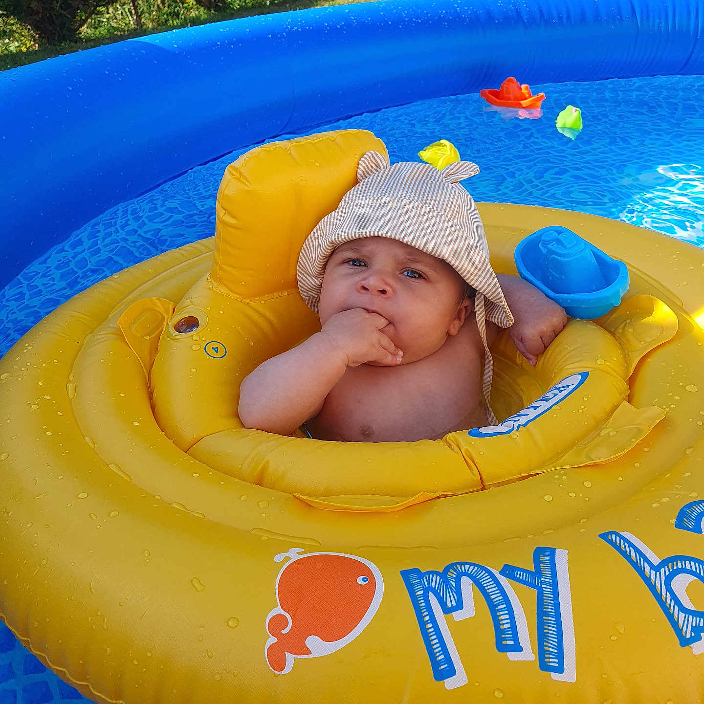 Ydris participe au concours pour gagner de l'argent avec cette photo : baby, backyard, blue, child, cute, face, hand, hat, infant, inflatable_float, outdoor, pool, relaxing, sitting, summer, sunny, swimming_pool, toy, water, yellow