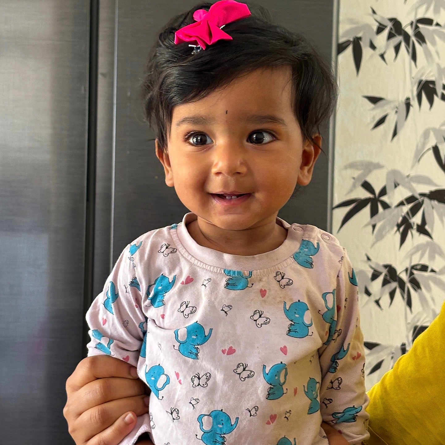 Mokshith joined the competition — help win amazing prizes! baby, black_hair, child, cute, elephant_print, face, hand, happy, holding, indoor, long_sleeve_shirt, patterned_clothing, person, pink_bow, portrait, sitting, smiling, toddler, wallpaper, yellow_sleeve