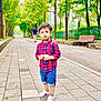 toddler, child, boy, plaid_shirt, denim_shorts, white_shoes, sidewalk, tree, greenery, bench, park, outdoor, person, walking, urban, casual_clothing, daylight, curious, cute, standing