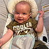 baby, infant, child, smiling, face, green_clothing, camouflage_pants, baby_seat, cushion, elephant_design, indoor, carpet, happy, cute, comfort, person, portrait, young_child, clothing, seatbelt