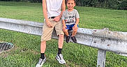 Jaydence is registered to the contest to win money with this photo: adult, baseball, baseball_bat, cap, casual_clothing, child, daylight, family, grass, guardrail, nature, outdoor, park, portrait, shorts, sitting, smiling, sneakers, sports, trees