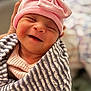 baby, newborn, smiling, pink_hat, bow, striped_blanket, swaddled, closeup, peaceful, infant, cute, sleepy, soft_lighting, portrait, hand, cozy, indoors, warm, adorable, child