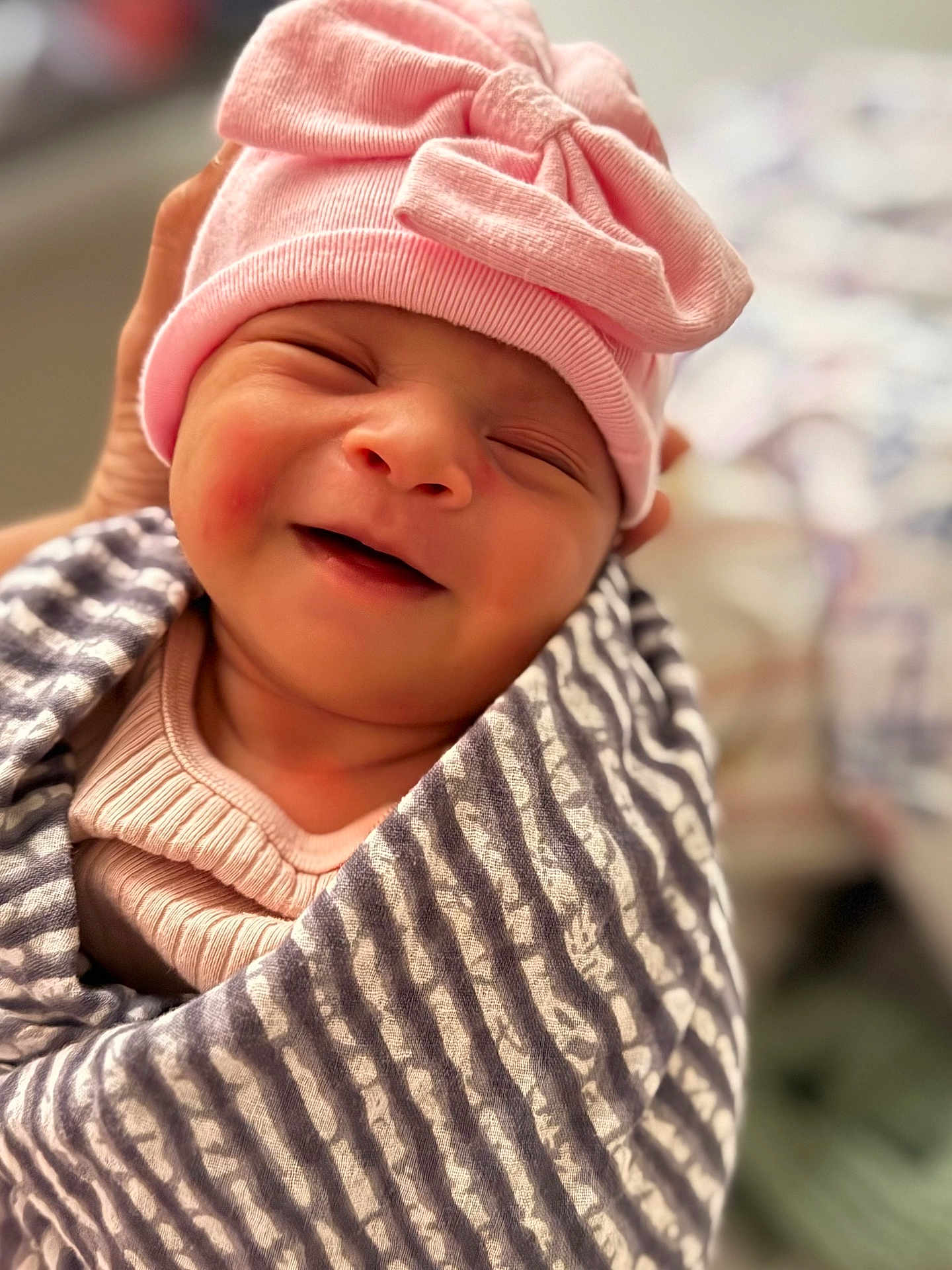 Ria is registered to the contest to win money with this photo: baby, newborn, smiling, pink_hat, bow, striped_blanket, swaddled, closeup, peaceful, infant, cute, sleepy, soft_lighting, portrait, hand, cozy, indoors, warm, adorable, child