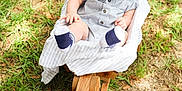 Brayden is registered to the contest to win money with this photo: baby, infant, child, outdoor, grass, wood, rocking_chair, clothing, socks, striped_outfit, nature, sunlight, seat, person, baby_boy, head, face, hands, ground, daytime