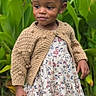 child, toddler, girl, portrait, outdoor, garden, plants, flowers, floral_dress, cardigan, pink_bow, braids, smiling, standing, shoes, grass, fashion, natural_light, full_body, safe