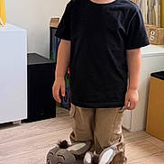 Logan joined the competition — help win amazing prizes! child, boy, smile, indoor, slippers, donkey_slippers, black_tshirt, khaki_pants, wooden_floor, curtains, lamp, toy, happy, standing, casual_clothing, home, playful, cute, young_child, portrait