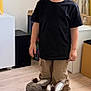 child, boy, smile, indoor, slippers, donkey_slippers, black_tshirt, khaki_pants, wooden_floor, curtains, lamp, toy, happy, standing, casual_clothing, home, playful, cute, young_child, portrait