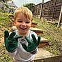 Logan is registered to the contest to win money with this photo: child, boy, smiling, gloves, green_gloves, gardening, outdoor, backyard, steps, fence, grass, cloudy_sky, pants, long_sleeve_shirt, happy, person, young_child, playful, casual_clothing, daytime
