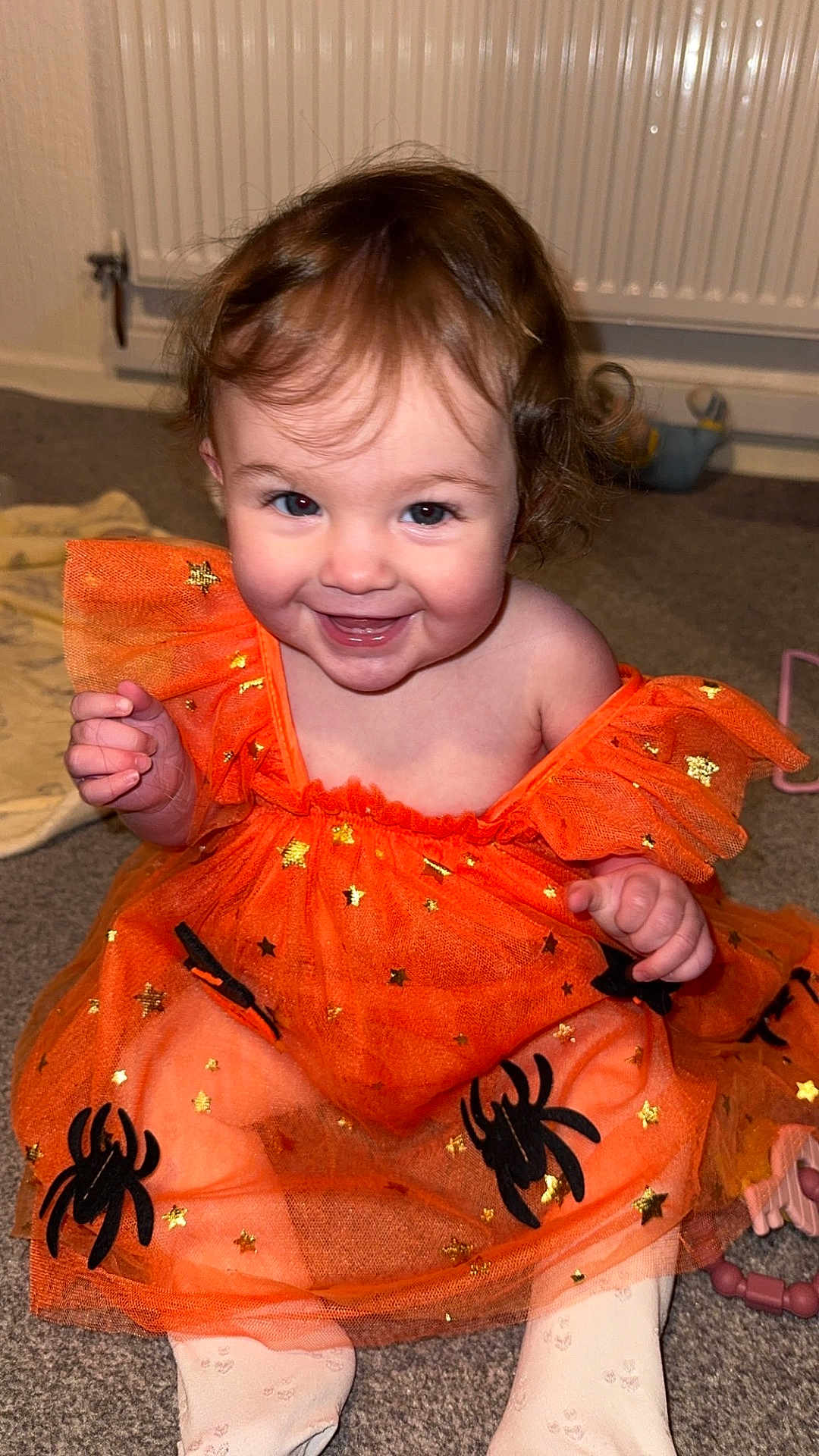 Averie-Grace joined the competition — help win amazing prizes! toddler, child, orange_dress, spiders, stars, smiling, happy, indoor, carpet, toy, radiator, cute, sitting, baby, face, person, clothing, legs, hands, curly_hair