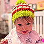 toddler, child, hat, knitted_hat, colorful, pink_sweater, butterfly_print, face, tongue_out, smile, indoor, blurred_background, cute, happy, person, young_child, baby, soft_lighting, cozy, playful