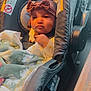 baby, blanket, bow, car_interior, car_seat, child, clothing, cute, face, hand, headband, indoors, infant, person, portrait, seat_belt, sitting, soft_fabric, warm_light, young_child