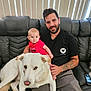 Luc is registered to the contest to win money with this photo: baby, man, dog, couch, tattoo, red_shirt, leather, indoor, family, pet, smile, person, blinds, phone, casual, seated, tattoos, hand, foot, home