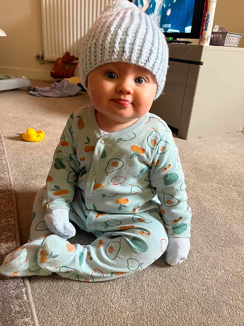 Denny James joined the competition — help win amazing prizes! baby, child, infant, onesie, hat, carpet, indoor, toy, rubber_duck, face, expression, cute, sitting, home, cozy, knit_hat, patterned_clothing, tongue_out, soft_light, domestic