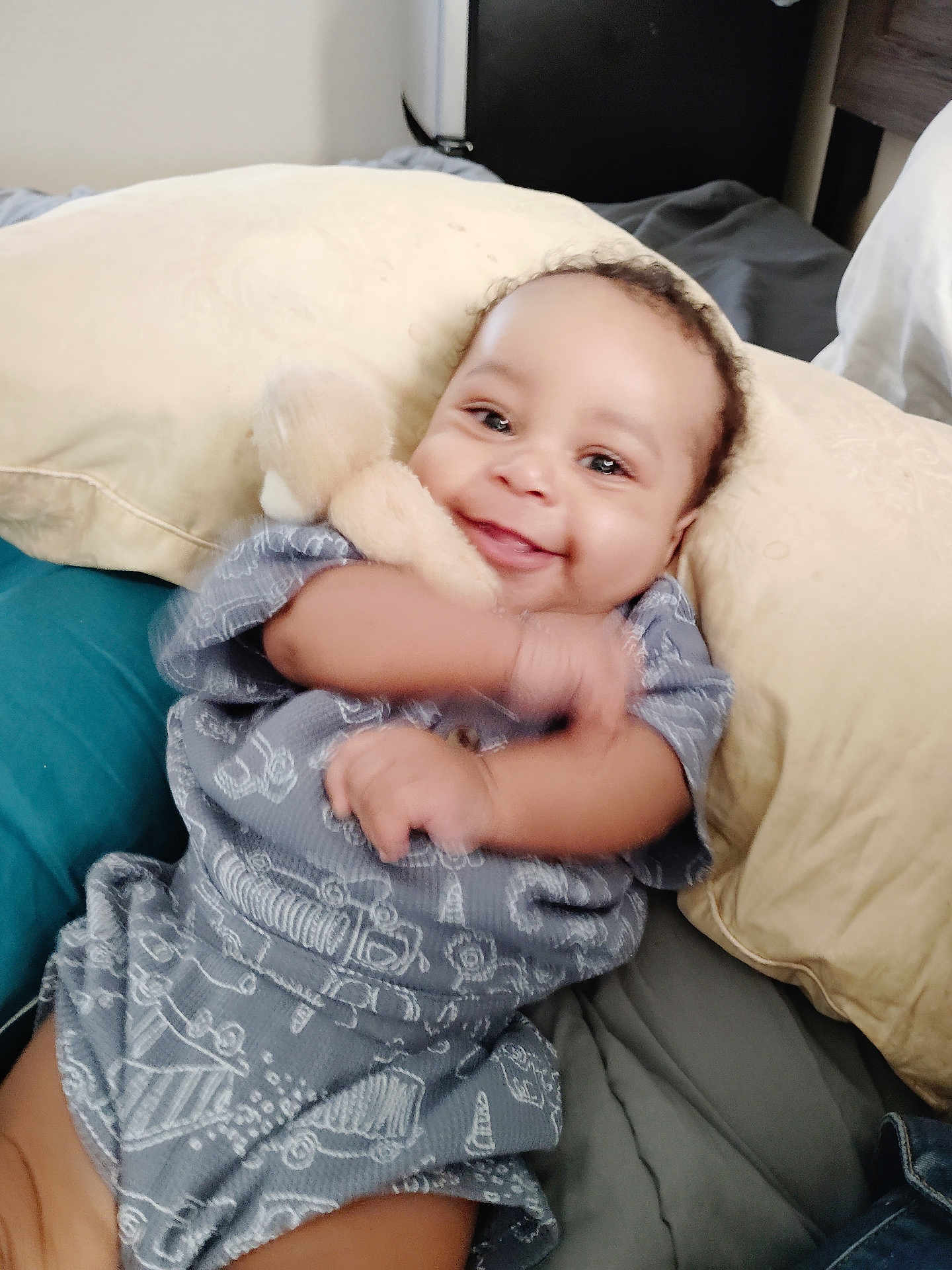 Tru joined the competition — help win amazing prizes! baby, infant, smiling_baby, smile, plush_toy, stuffed_animal, pillow, blanket, bed, onesie, arm_motion, chubby_cheeks, bright_eyes, indoor, portrait, happy, cozy, fabric_pattern, hand, candid