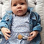 baby, infant, child, headband, bow, denim_jacket, blue_dress, floral_pattern, pacifier_clip, quilted_blanket, star_pattern, hands, face, eyes, cute, lying_down, soft_light, clothing, portrait, indoors