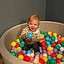 ball_pit, blonde_hair, casual_clothing, child, colorful_balls, curious, floor, fun, happy, indoor, person, play, playroom, round_pit, smile, sock, toddler, toy, wooden_toy, young_child