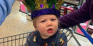 River is registered to the contest to win money with this photo: toddler, child, shopping_cart, hat, mardi_gras, grocery_store, dr_pepper, beverage, cart, clothing, sweater, pants, adult_hand, floor, shelf, box, plastic_jug, person, indoor, curious