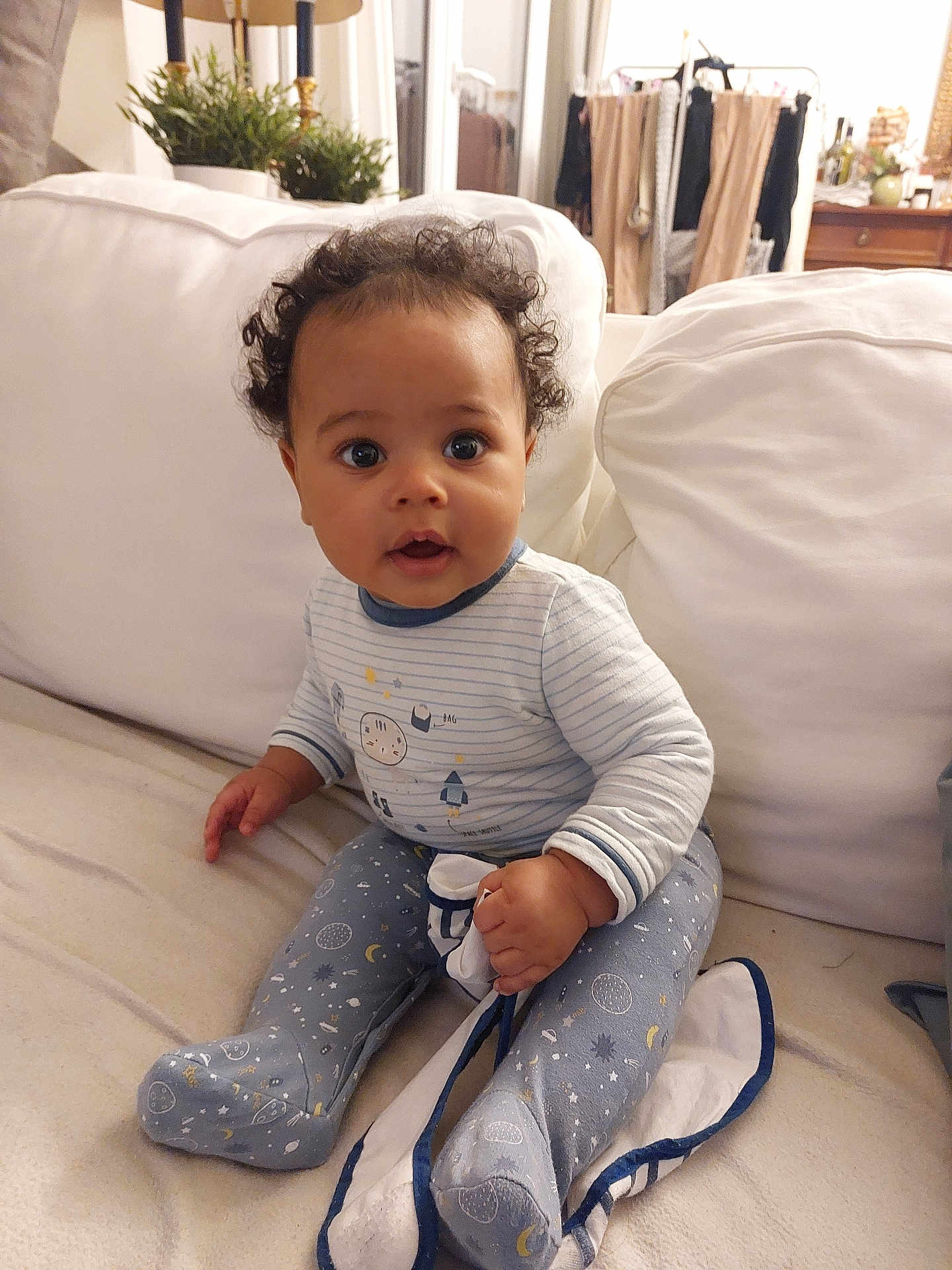 Ewan participe au concours pour gagner de l'argent avec cette photo : baby, child, indoor, couch, blanket, curly_hair, pajamas, face, person, furniture, plant, home, seated, cozy, cute, expression, hand, footed_pajamas, living_room, smile