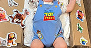 Yeshúa joined the competition — help win amazing prizes! baby, child, smiling, toy_story, romper, blue_clothing, cardboard_box, stickers, wooden_floor, indoor, happy, cute, infant, person, playful, decorations, blanket, sitting, smile, young_child