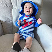 Yeshúa is registered to the contest to win money with this photo: baby, child, smiling, blue_hat, striped_clothing, lobster_design, armchair, indoor, happy, cute, infant, footwear, baby_clothes, hat, person, seated, portrait, furniture, light, texture