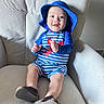 Yeshúa is registered to the contest to win money with this photo: baby, child, smile, hat, blue_clothing, striped, lobster_design, chair, armchair, footwear, happy, indoors, person, cute, infant, sitting, portrait, comfortable, texture, bright