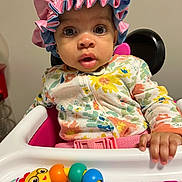 Aziah joined the competition — help win amazing prizes! baby, child, high_chair, bonnet, colorful_clothing, toy, rainbow_toy, floral_pattern, hand, face, wide_eyes, curious_expression, indoor, infant, seat_belt, pink, blue, yellow, orange, playful