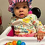 baby, child, high_chair, bonnet, colorful_clothing, toy, rainbow_toy, floral_pattern, hand, face, wide_eyes, curious_expression, indoor, infant, seat_belt, pink, blue, yellow, orange, playful