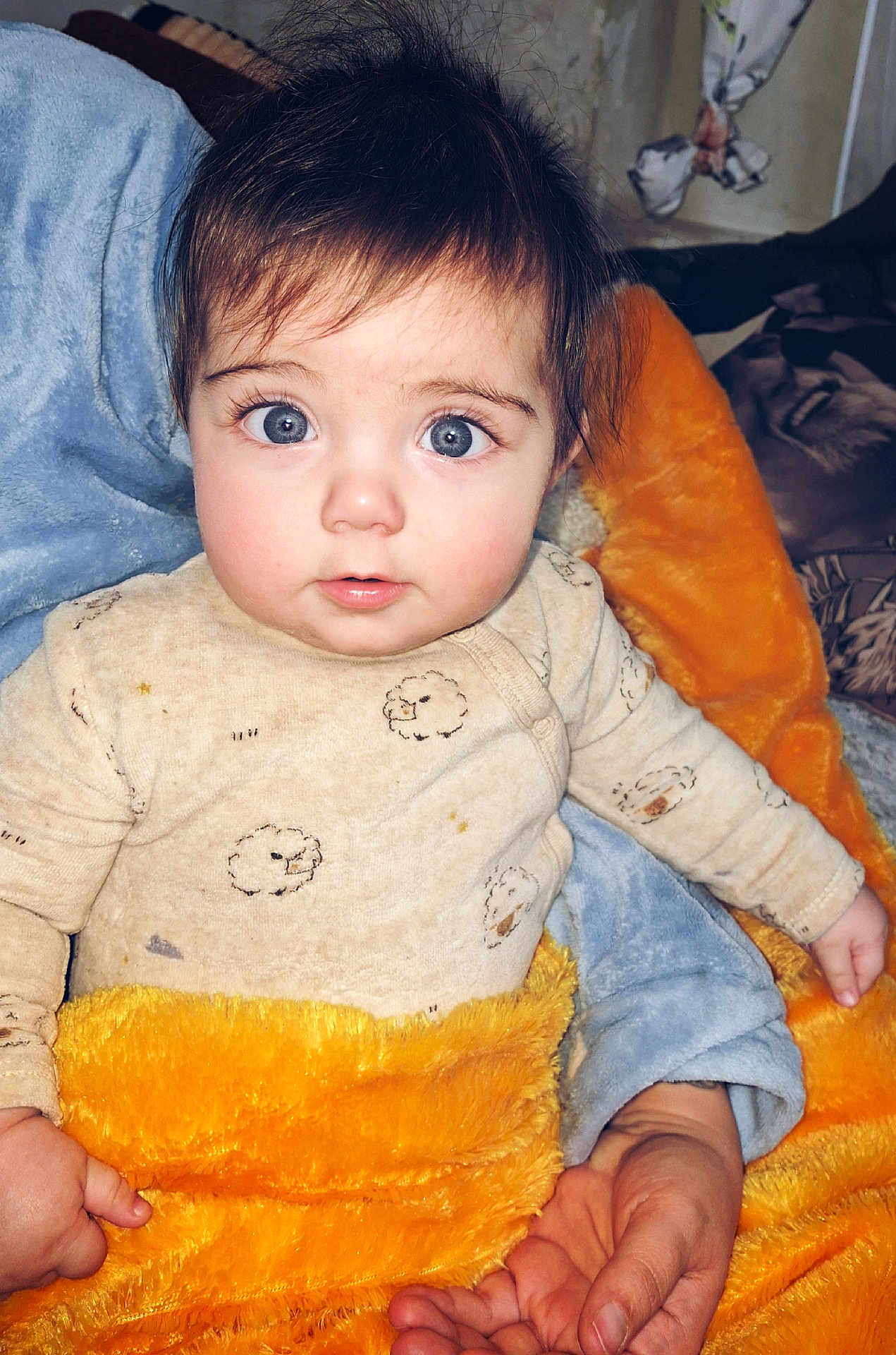 Rubí is registered to the contest to win money with this photo: baby, infant, child, big_eyes, blue_eyes, surprised_expression, onesie, blanket, orange_blanket, blue_blanket, cozy, plush, bed, portrait, hair, eyelashes, hand, skin, indoor, adorable