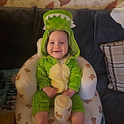 Aidan is registered to the contest to win money with this photo: baby, child, couch, cozy, cute, dinosaur_costume, face, green_clothing, happy, headwear, home, indoor, infant, inflatable_chair, onesie, plush, portrait, seated, smiling, teddy_bear_prints