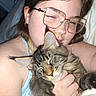 person, woman, cat, kitten, tabby, pet, cuddling, sleeping, closed_eyes, glasses, portrait, selfie, indoors, bedroom, blanket, hand, bracelet, earrings, long_hair, affection