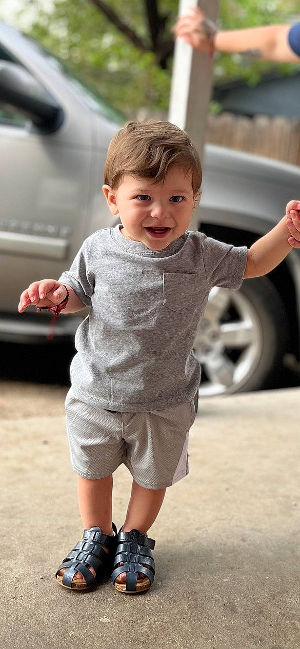 Benjamin is registered to the contest to win money with this photo: automotive_design, automotive_tire, car, finger, gesture, hairstyle, hand, happy, joint, mammal, person, shorts, skin, sleeve, smile, standing, style, tire, toddler, vehicle