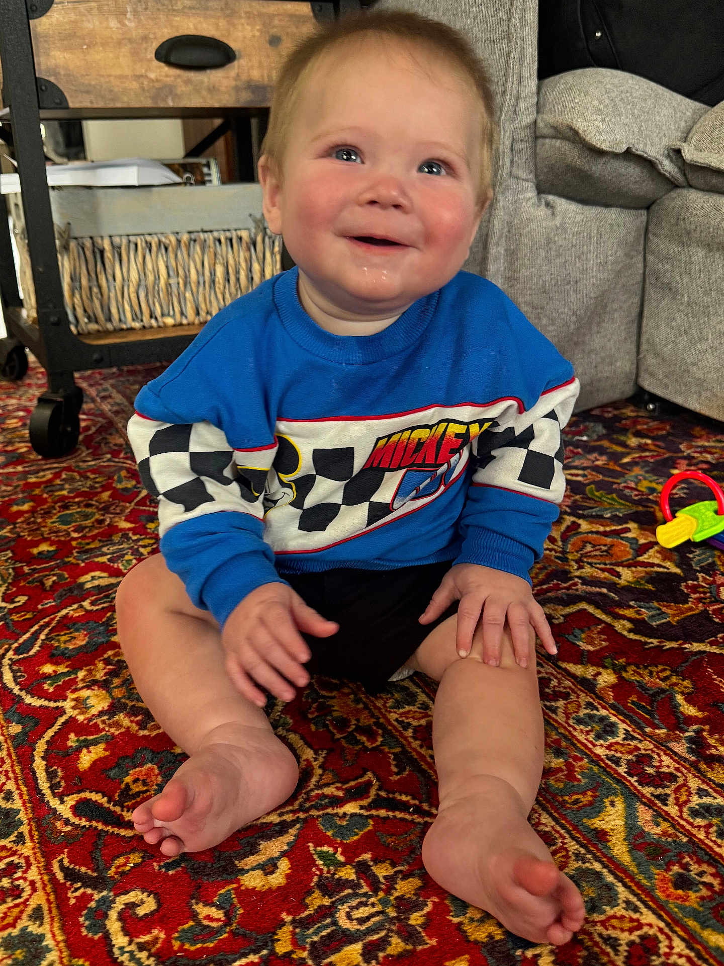 Oakley joined the competition — help win amazing prizes! baby, child, sitting, smiling, blue_sweatshirt, mickey_mouse, carpet, rug, indoor, toy, furniture, couch, happy, cute, person, foot, hand, home, patterned_rug, cozy