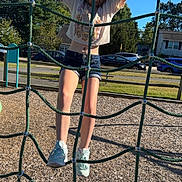 Niomi is registered to the contest to win money with this photo: child, climbing, playground, rope_net, outdoor, summer, shorts, tshirt, sneakers, wood_chips, trees, cars, houses, blue_sky, daylight, person, recreation, fun, activity, park
