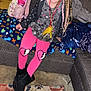 child, girl, braided_hair, pink_leggings, broken_heart, black_boots, couch, blanket, pillow, backpack, unicorn, carpet, indoor, smiling, home, casual_clothing, seated, colorful, happy, portrait