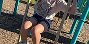 Niomi is registered to the contest to win money with this photo: child, girl, playground, climbing, ladder, outdoor, daytime, smiling, casual_clothing, shorts, tshirt, sneakers, woodchips, play_equipment, metal_bars, trees, sky, sunlight, happy, recreation