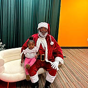 Siya is registered to the contest to win money with this photo: baby, child, santa_claus, adult, portrait, smiling, indoors, christmas, festive, red_suit, white_beard, santa_hat, couch, chair, curtain, orange_wall, carpet, family, holiday, photography