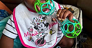 Cori joined the competition — help win amazing prizes! automotive, baby, bib, brown_skin, car_seat, child, closeup, curly_hair, disney, eyes, face, hand, indoor, infant, minnie_mouse, portrait, rattle, sitting, striped_shirt, toy