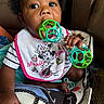Cori joined the competition — help win amazing prizes! baby, child, infant, portrait, sitting, car_seat, rattle, toy, bib, minnie_mouse, disney, striped_shirt, curly_hair, brown_skin, face, eyes, hand, indoor, automotive, closeup