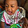 Cori is registered to the contest to win money with this photo: baby, child, infant, portrait, sitting, high_chair, smiling, open_mouth, curly_hair, dark_skin, bib, minnie_mouse, striped_clothing, toy, colorful_toy, indoor, home, close_up, happy, playtime