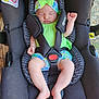 baby, car_seat, sleeping, headband, green_outfit, infant, child, safety_harness, wooden_floor, indoors, peaceful, cute, small_hands, small_feet, soft_skin, black_car_seat, resting, adorable, toddler, childcare