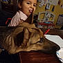 child, dog, table, tongue, playful, indoor, wood, toy, note, paper, pen, face, ear, room, background, brown, furniture, expression, cute, pet