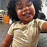 Kash is registered to the contest to win money with this photo: child, toddler, smiling, curly_hair, nike, shirt, indoor, living_room, couch, furniture, happy, person, portrait, cute, young, home, laughing, casual_clothing, skin, face