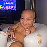 baby, infant, child, smiling, happy, portrait, sitting, high_chair, cushioned_seat, bear_pattern, indoor, home, television, relaxed, playful, bare_chested, baby_feet, close_up, flash_photography, family_photo