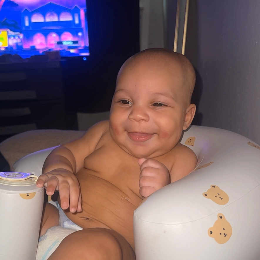 Kazire is registered to the contest to win money with this photo: baby, infant, child, smiling, happy, portrait, sitting, high_chair, cushioned_seat, bear_pattern, indoor, home, television, relaxed, playful, bare_chested, baby_feet, close_up, flash_photography, family_photo